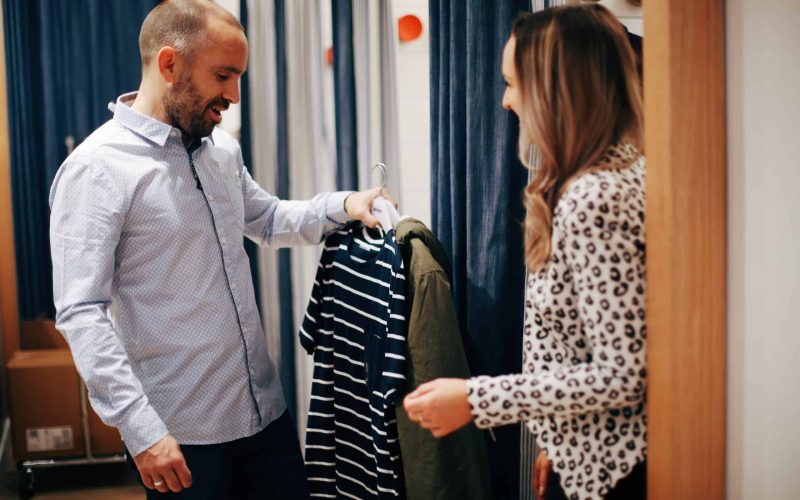 Hayley Cooper inspects clothes in a changing room with a male client. Hayley Cooper inspects clothes in a changing room with a male client.